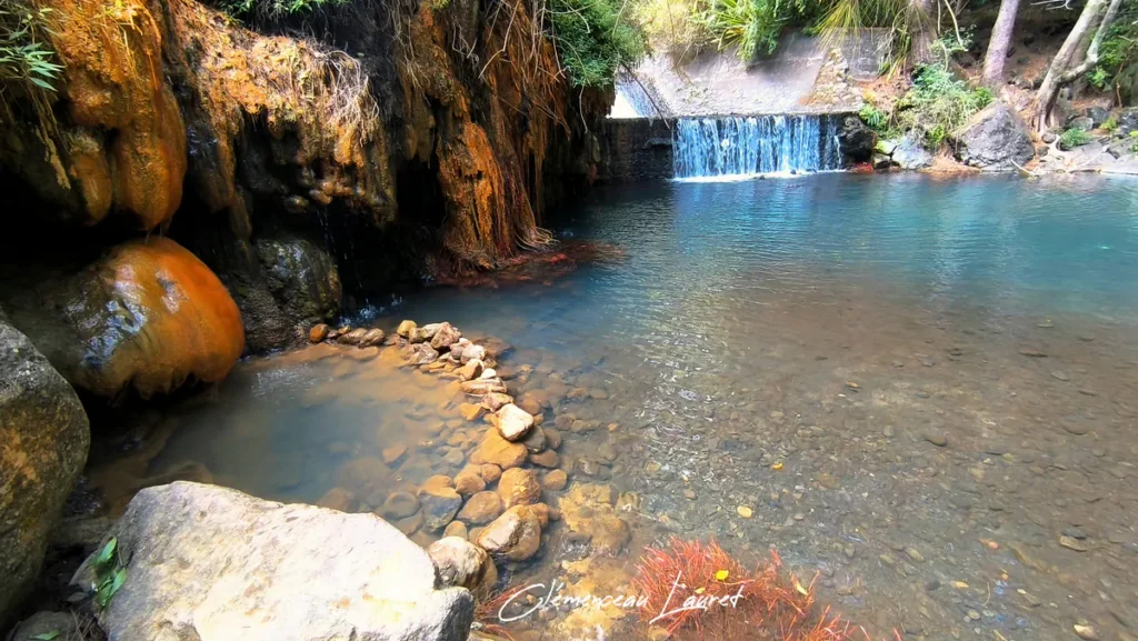 Petit bassin aménagé avec des galets au pied de dépôts de fer orangés aux anciens thermes de Cilaos par temps lumineux