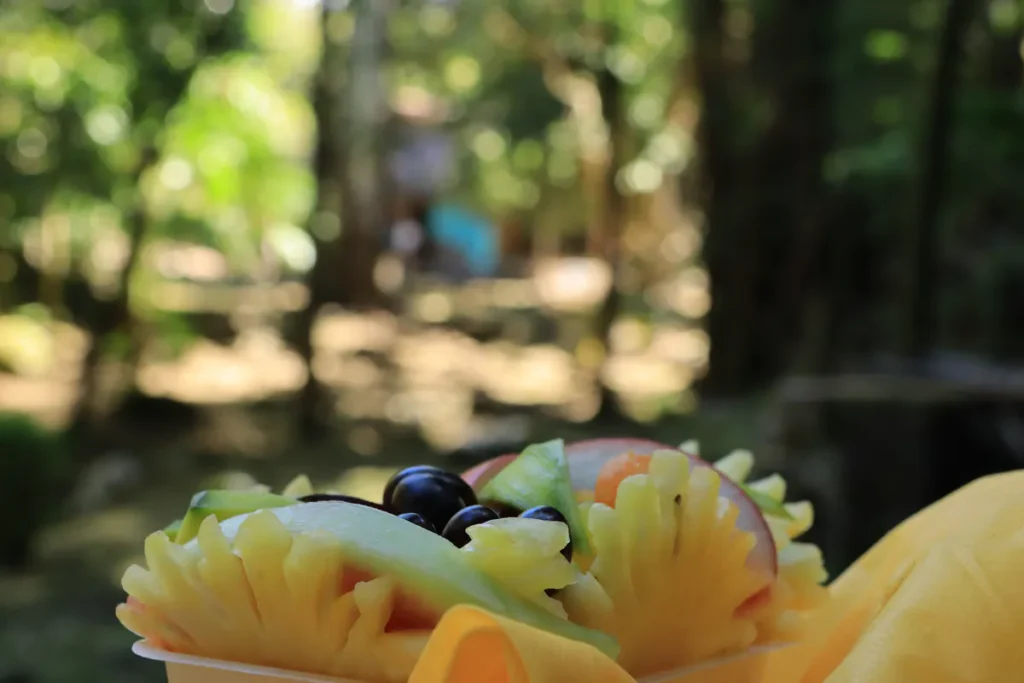 Barquette jaune garnie d'ananas Victoria, jamblons noirs et mangue verte sous la lumière naturelle à Saint-Pierre, La Réunion.