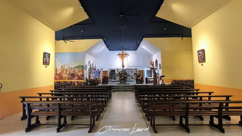 Nef centrale illuminée et bancs en bois alignés dans l'église aux Avirons à La Réunion sous un plafond sombre et chaleureux.