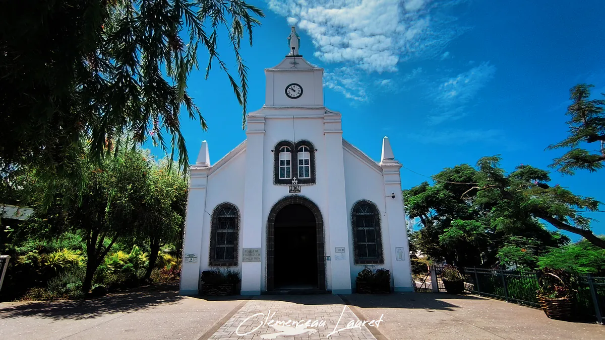 Façade principale blanche de l'église aux Avirons à La Réunion avec arcade en pierre basaltique sous un ciel bleu dégagé.
