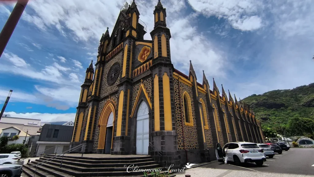 Autre angle de la façade avant et du clocher de l'église Notre-Dame de la Délivrance sous un ciel lumineux, à Saint-Denis, La Réunion — Photo : Clémenceau Lauret (CC BY-SA 4.0).