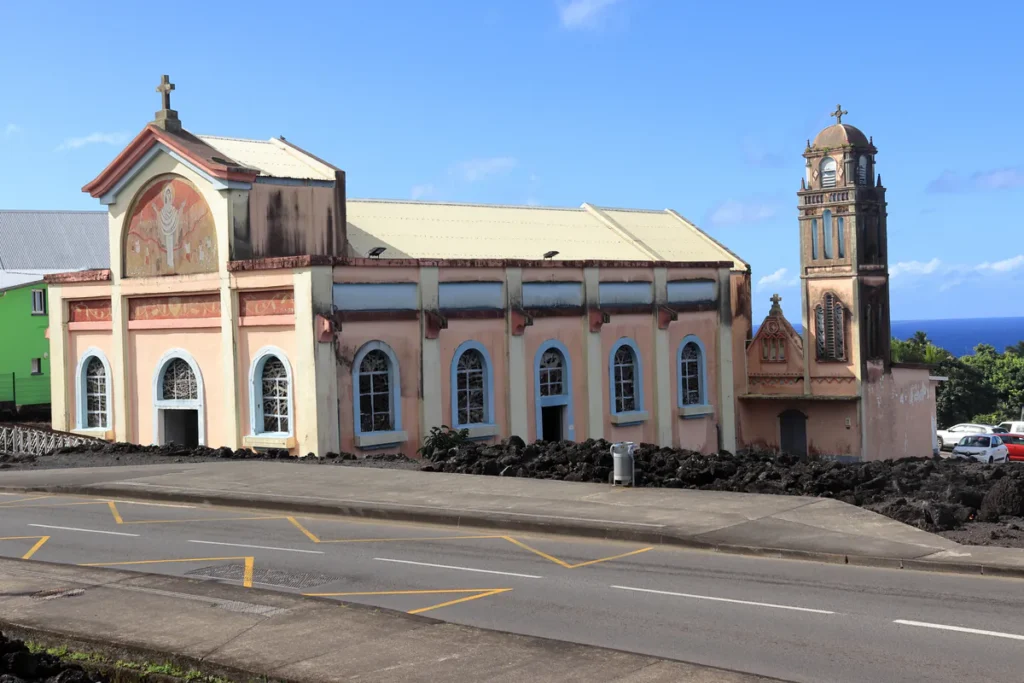 Église rose bordée de lave basaltique noire le long de la route à Piton Sainte-Rose sous un ciel ensoleillé.