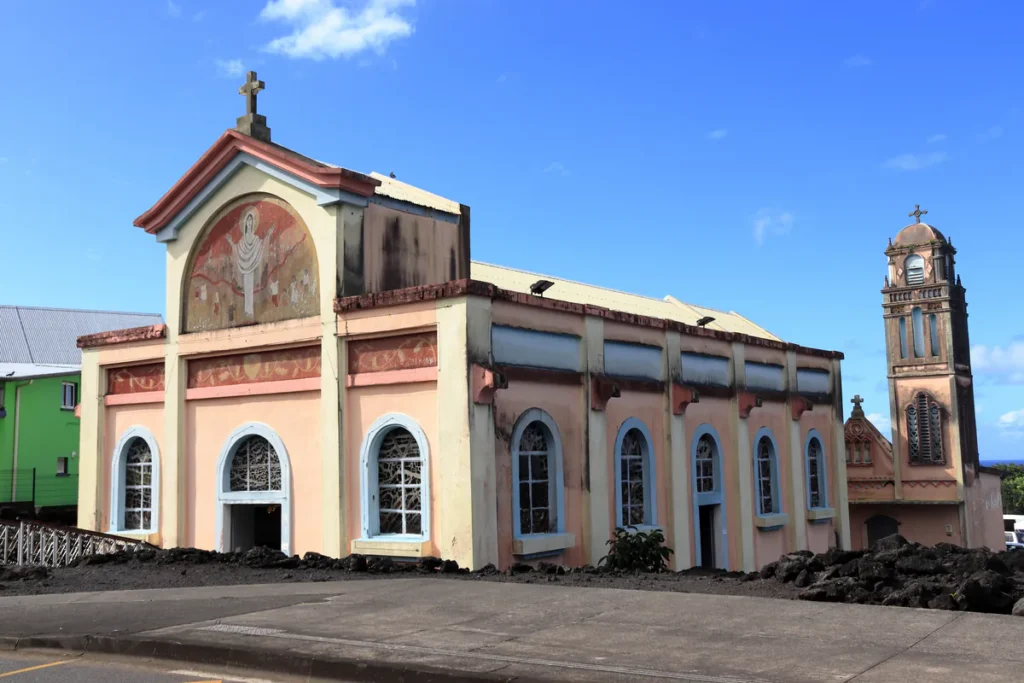 Vue en contre-plongée de l'église Notre-Dame des Laves et son clocher entourés de gratons de lave à Sainte-Rose.