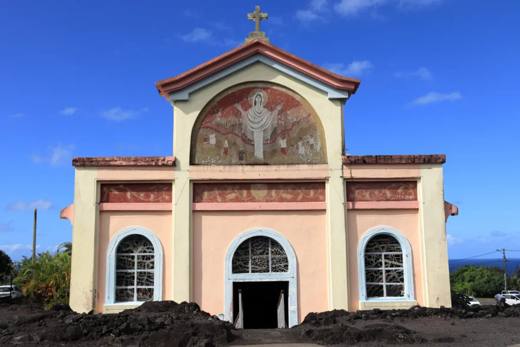 Façade symétrique de l'église Notre-Dame des Laves enserrée par la roche volcanique noire à Sainte-Rose.