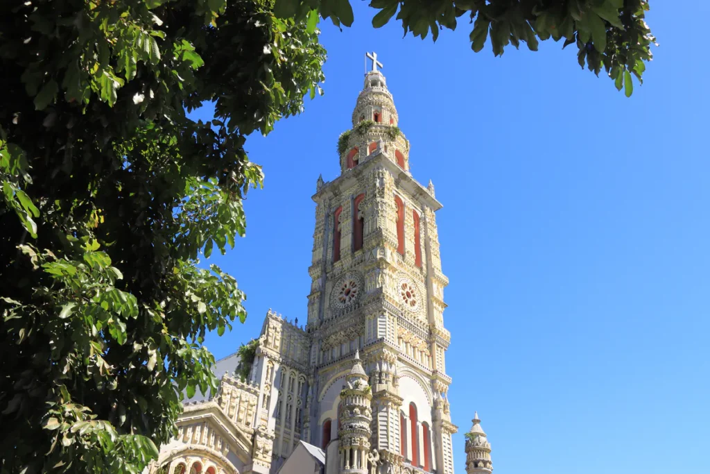 Clocher ouvragé de l'église Sainte-Anne à Saint-Benoît encadré par des feuillages tropicaux sous le soleil.