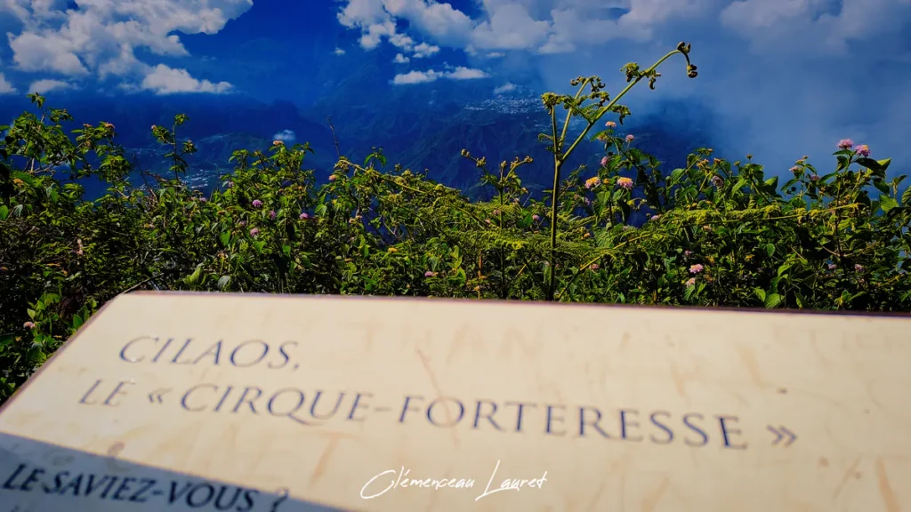 Panneau d'information touristique en bois intitulé "CILAOS, LE « CIRQUE-FORTERESSE »", situé à La Fenêtre des Makes à Saint-Louis, avec la végétation et les montagnes du cirque en arrière-plan.