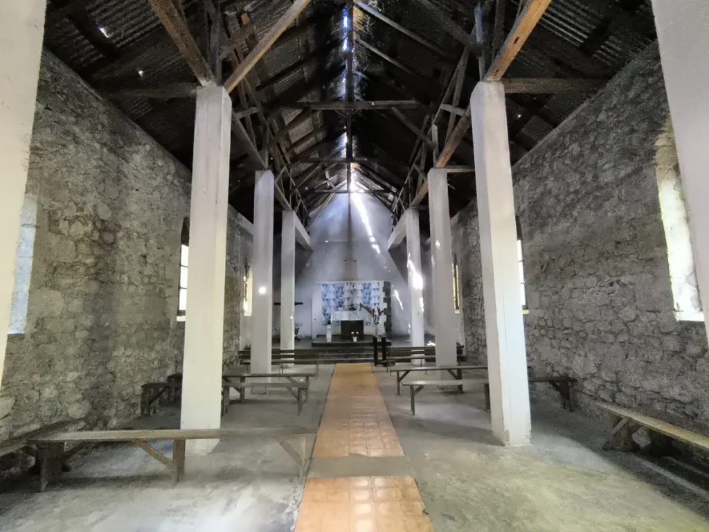 Intérieur de la chapelle de l'Îlet Bethléem à Saint-Benoît avec bancs en bois, piliers blancs et rais de lumière.