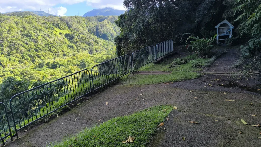 Sentier asphalté bordé d'un garde-corps métallique surplombant une vallée verdoyante à Saint-Benoît sous une lumière tamisée