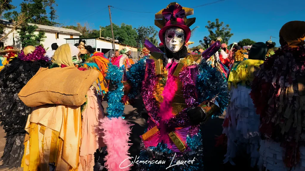 Vue rapprochée d'un défilant en costume violet et doré entouré d'autres participants recouverts de sac de toile et de bandes de plastique sombres.