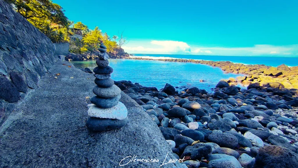 Cairn de galets basaltiques au bord du bassin naturel de Manapany-les-Bains à Saint-Joseph sous une lumière vive.