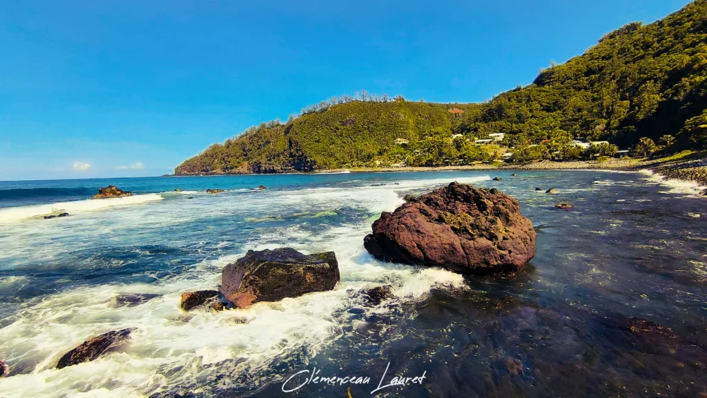 Vue panoramique de la baie de Manapany-les-Bains entourée de sa haute falaise verdoyante et de rochers volcaniques.