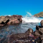 Éclat d'eau sous une vague se brisant violemment contre la digue de roches basaltiques du bassin de Manapany-les-Bains.