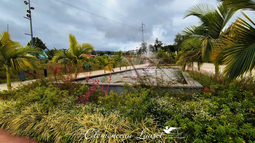 Massif de plantes colorées en bordure d'un grand bassin rectangulaire à jets d'eau sous un ciel nuageux au Parc des Palmiers à Le Tampon, Île de La Réunion. Photo : Clémenceau Lauret (CC BY-SA 4.0).