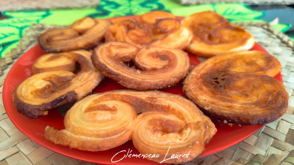 Plan d'ensemble montrant une assiette de palmiers feuilletés aux nuances dorées et ambrées, posée sur un dessous de plat traditionnel en fibres de vacoa tressées à Saint-Joseph, La Réunion. Prise de vue et photographie réalisées par Clémenceau Lauret.