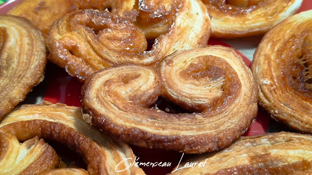 Gros plan détaillé sur les alvéoles du feuilletage doré et le caramel brillant d'un palmier artisanal cuit au four, disposé sur un plat de présentation rouge à Saint-Joseph, La Réunion. Prise de vue et photographie réalisées par Clémenceau Lauret.