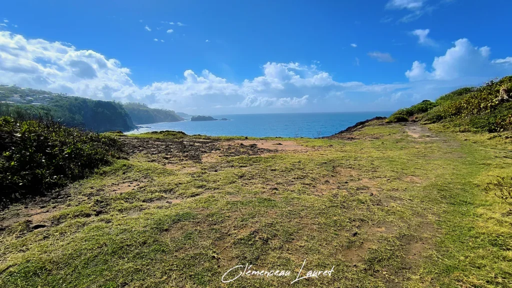 Sentier herbeux au sommet d'une falaise littorale à Petite-Île ouvrant sur l'océan Indien par temps ensoleillé et nuageux.