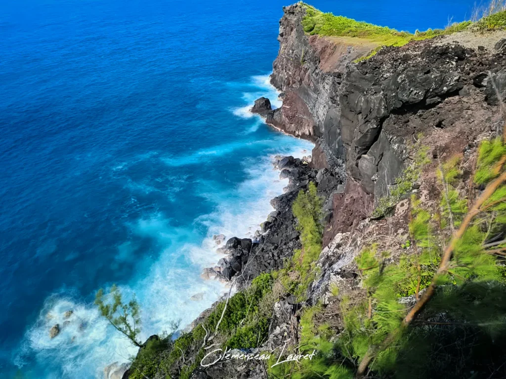 Vue en contre-plongée d'une falaise basaltique abrupte battue par l'écume blanche de l'océan Indien à Petite-Île sous une vive lumière.