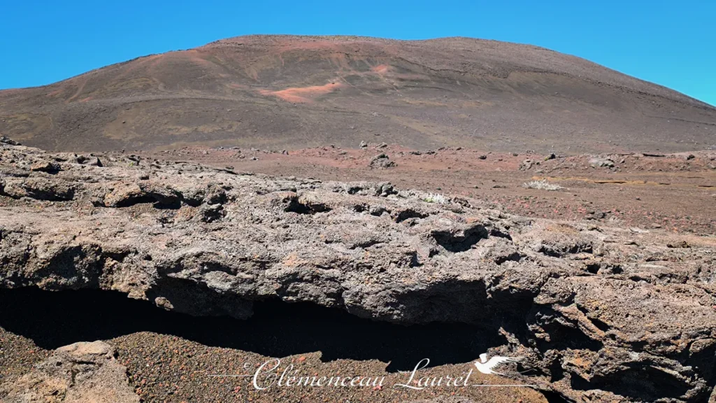 Formation rocheuse volcanique texturée au premier plan avec en arrière-plan le dôme rougeoyant des reliefs de la Plaine des Sables à La Réunion, Clémenceau Lauret, CC BY-SA 4.0.