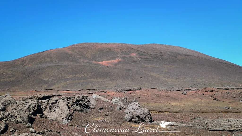 Vue de face d'un cône volcanique aux teintes ocres et cuivrées dominant les étendues de la Plaine des Sables à La Réunion, Clémenceau Lauret, CC BY-SA 4.0.