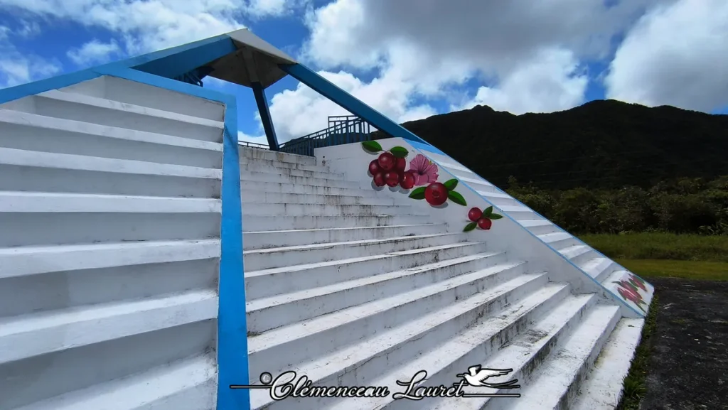 Gros plan sur l'escalier latéral et les fresques peintes de fruits rouges sous un ciel nuageux à La Plaine-des-Palmistes.