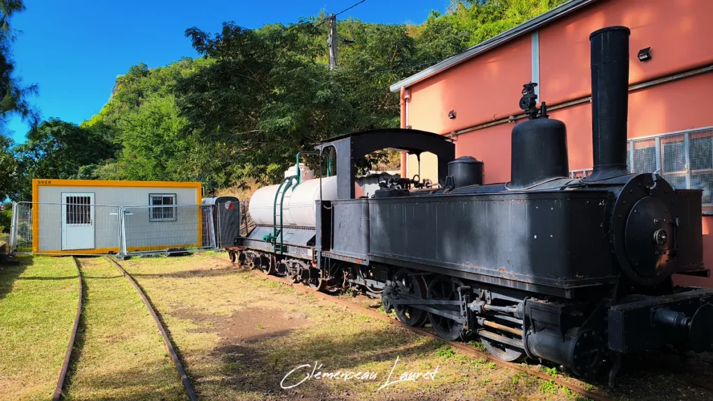Locomotive à vapeur noire du Train Lontan garée sur les rails de la Grande Chaloupe à La Possession sous un ciel ensoleillé.